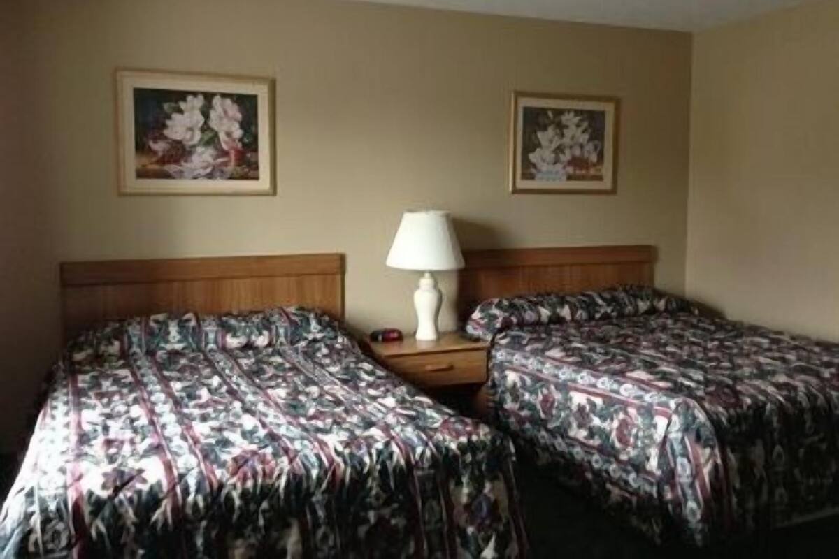 A hotel room with two beds, a nightstand with a lamp, and two framed pictures on the wall.