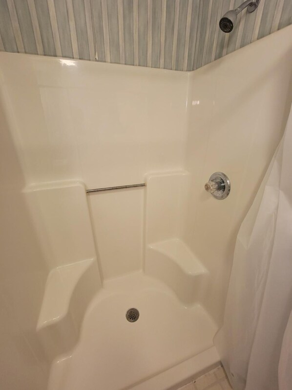 A white bathtub with a showerhead, a drain, and a metal bar.