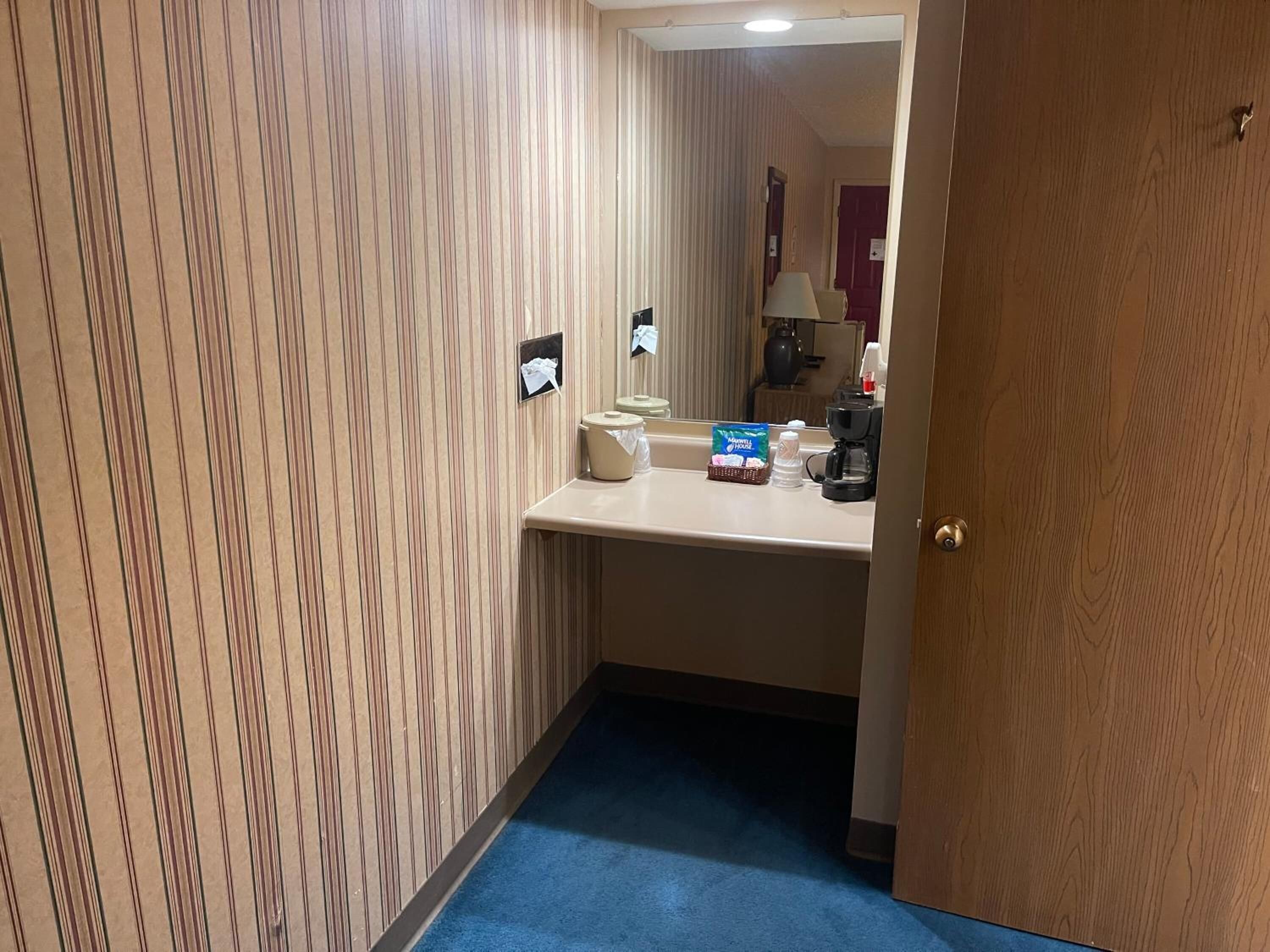 Un baño de hotel con papel tapiz a rayas, un lavamanos, un espejo, un dispensador de toallas y una cafetera.