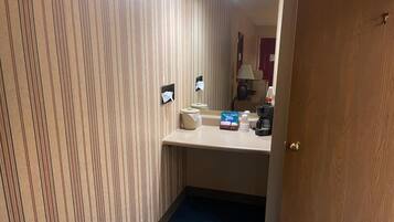 Un baño de hotel con papel tapiz a rayas, un lavamanos, un espejo, un dispensador de toallas y una cafetera.