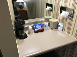 Casa de banho de hotel com lavatório, máquina de café, caixa de lenços de papel e lixeira.
