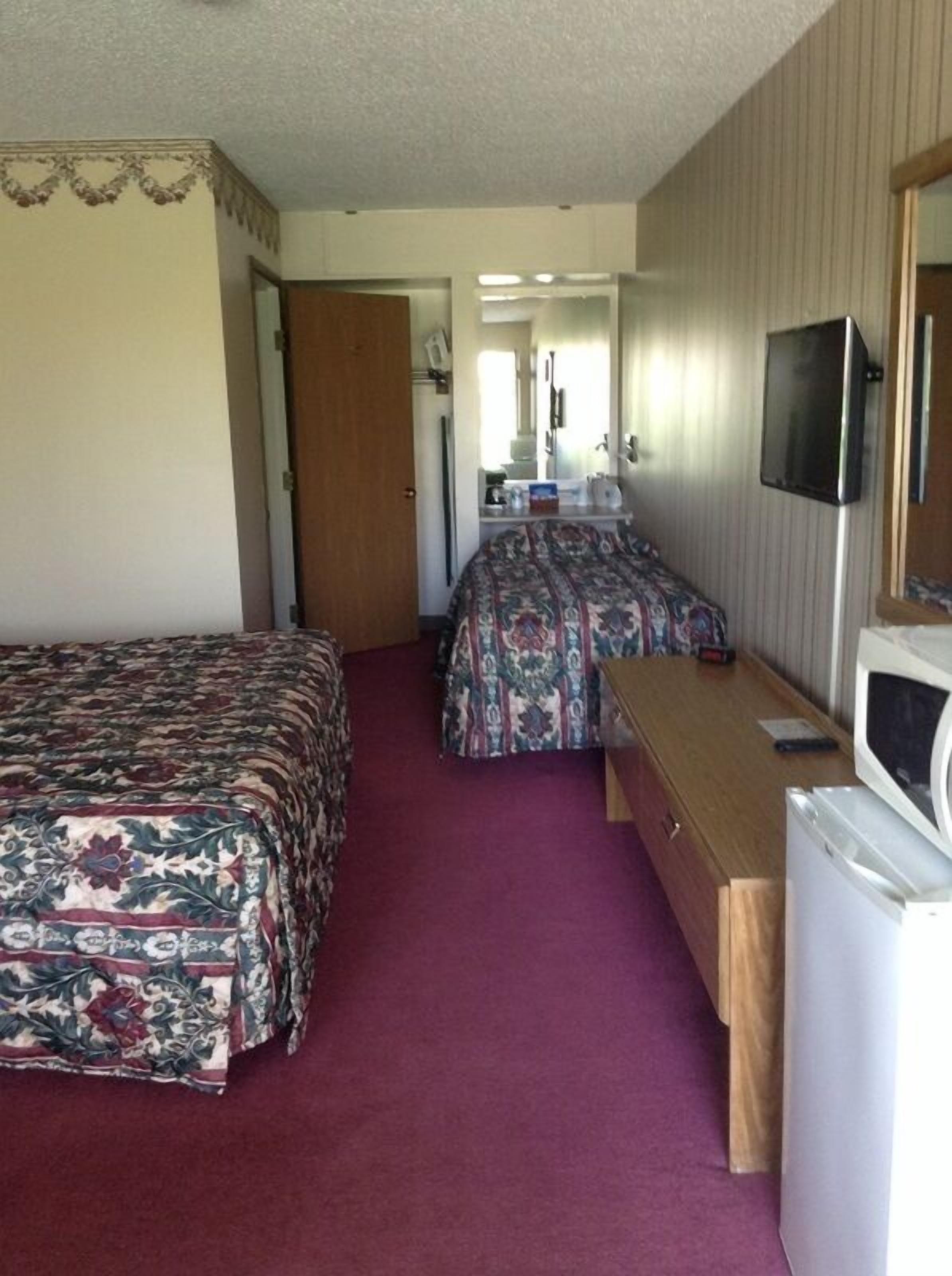 A compact hotel room with two beds, a desk, a television, and a microwave.