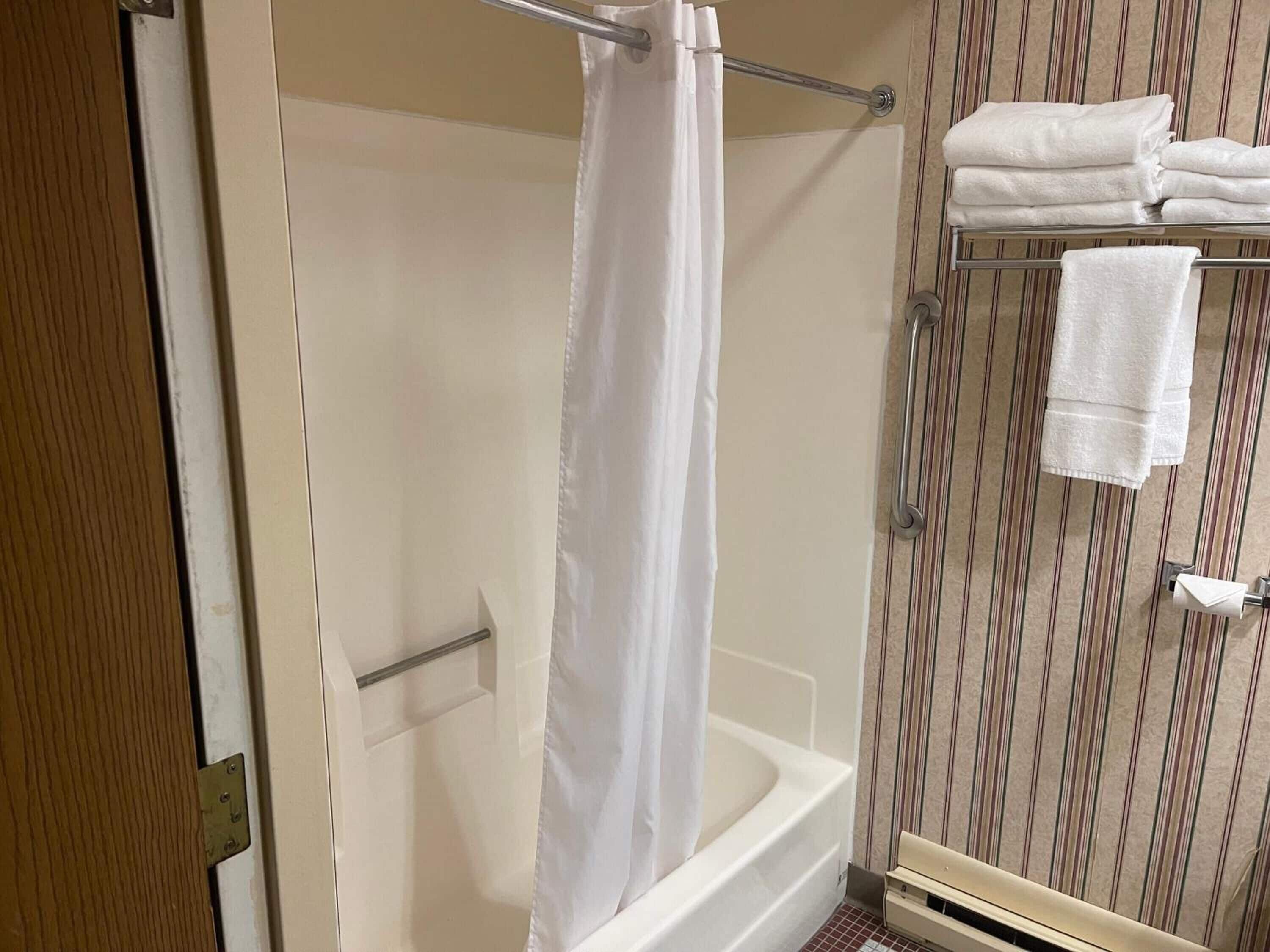 A shower with a white curtain, a towel rack with folded towels, and a striped wallpaper background.