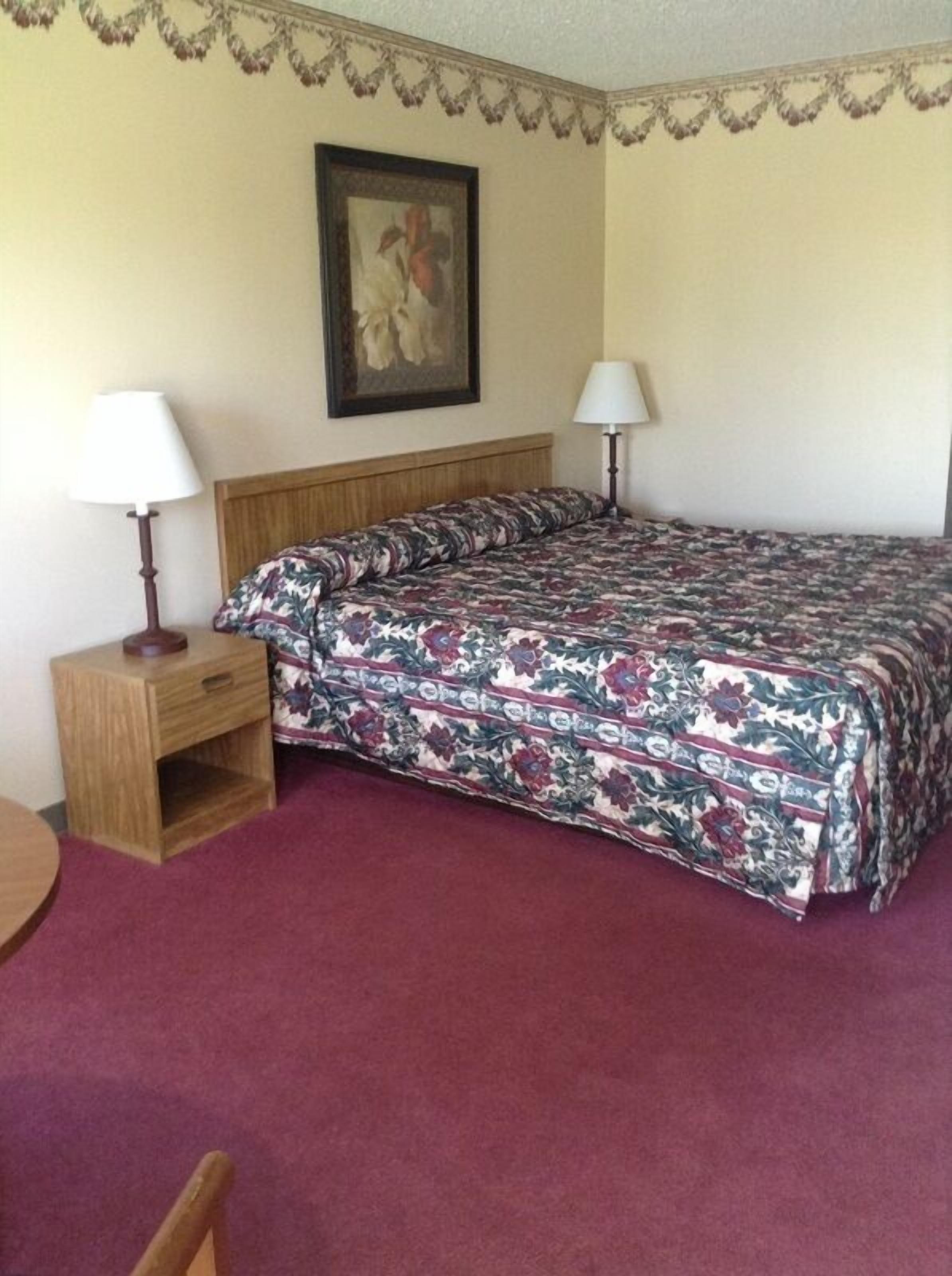 Una habitación de hotel con una cama, dos mesitas de noche, una silla y un cuadro en la pared.