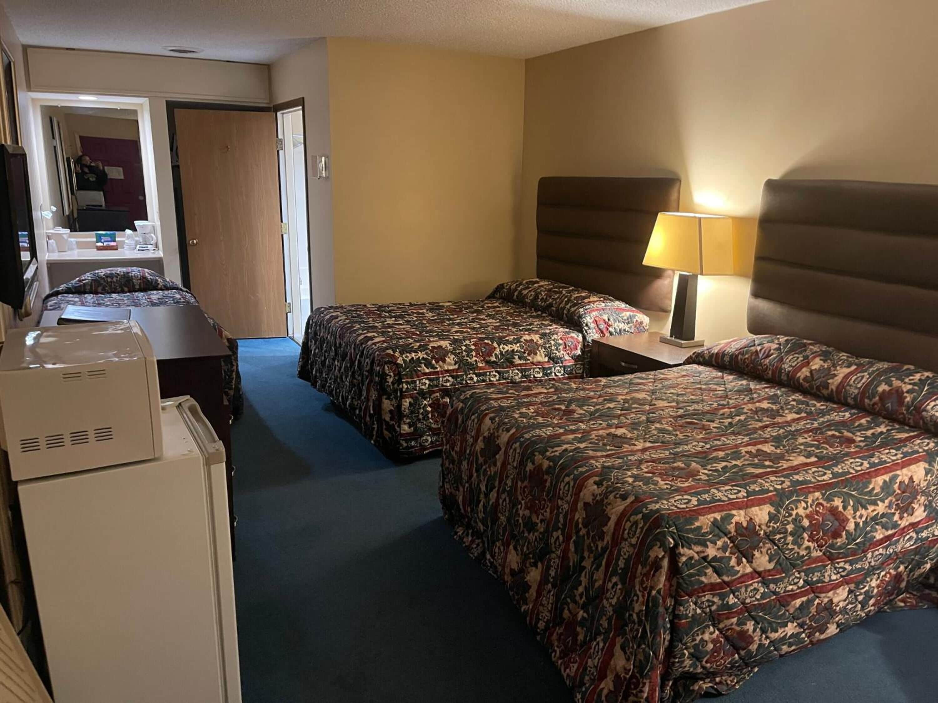 Quarto de hotel com duas camas, uma escrivaninha, uma cadeira, um abajur e uma televisão.