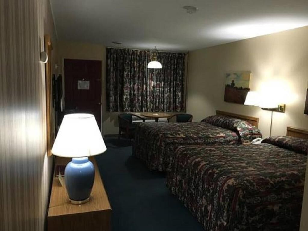 Ein Hotelzimmer mit zwei Betten, einem Schreibtisch, einem Stuhl, einer Lampe und einem Vorhang.