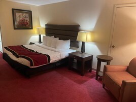 Quarto de hotel com uma cama, duas mesas de cabeceira com abajures, uma cadeira e uma porta.