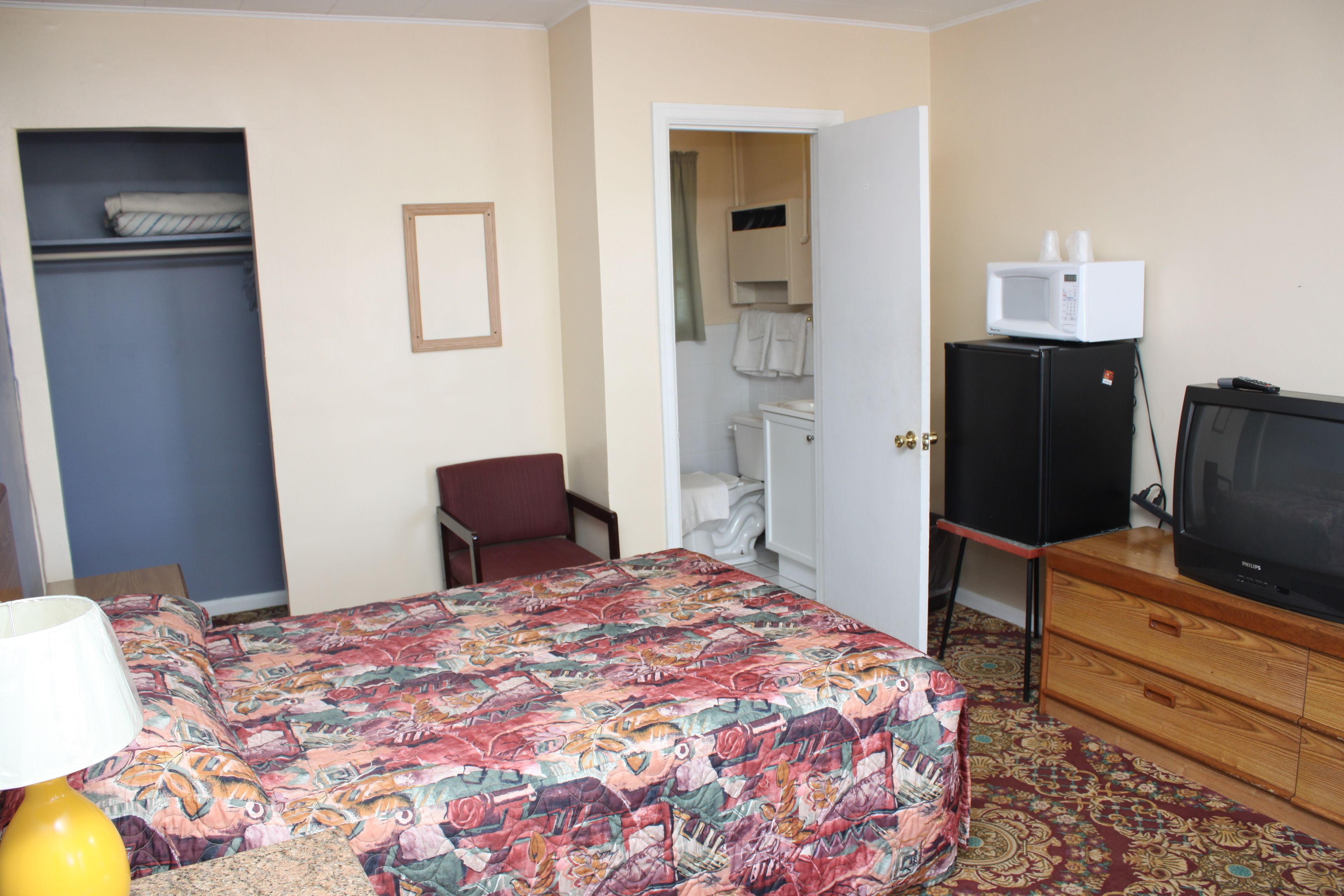 A hotel room with a bed, a desk, a chair, a wardrobe, a bathroom, and a television.
