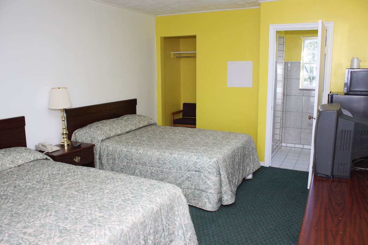 A hotel room with two beds, a desk with a computer, a telephone, and a lamp.