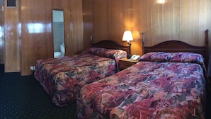 Habitación de hotel con dos camas, un escritorio, una silla, una lámpara y un baño visible a través de una puerta abierta.