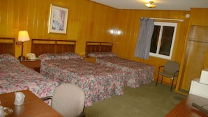 Habitación de hotel con tres camas individuales, un escritorio con silla, una lámpara y una ventana con cortinas.