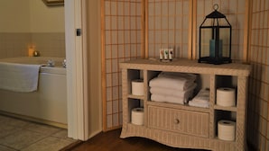 A bathroom with a bathtub, a wicker vanity with towels and toiletries, and a mirror on the wall. - Meris Gardens Bethany (Bethany Beach)