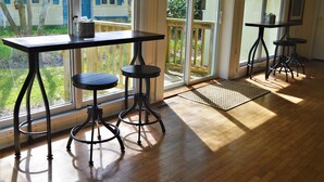 A sunlit room with a large window, a wooden table, and two stools. - Meris Gardens Bethany (Bethany Beach)