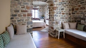 A room with stone walls, a wooden floor, a bed, a sofa, and a small table with a lamp. - Amanita Guesthouse (Zagora-Mouresi)
