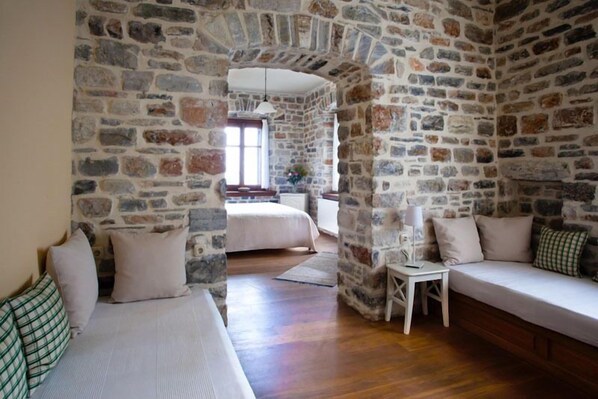 Quarto com paredes de pedra, piso de madeira, cama, sofá e uma pequena mesa com abajur.