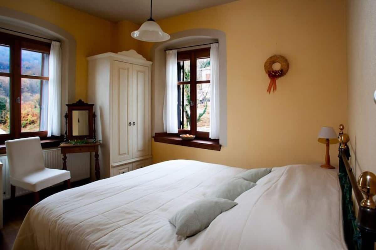 A bedroom with a bed, a chair, a desk, a wardrobe, and a window with a view.