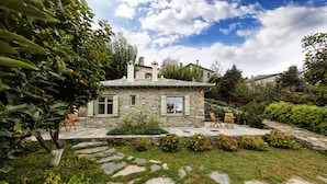 A stone house with a stone patio, surrounded by greenery and a stone pathway. - Amanita Guesthouse (Zagora-Mouresi)
