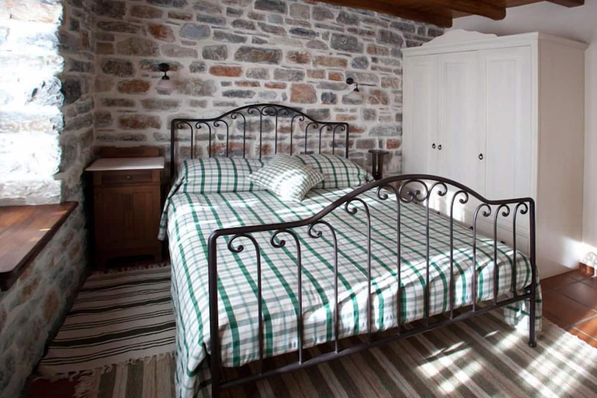A room with a stone wall, a metal bed frame, a wooden nightstand, and a white wardrobe.