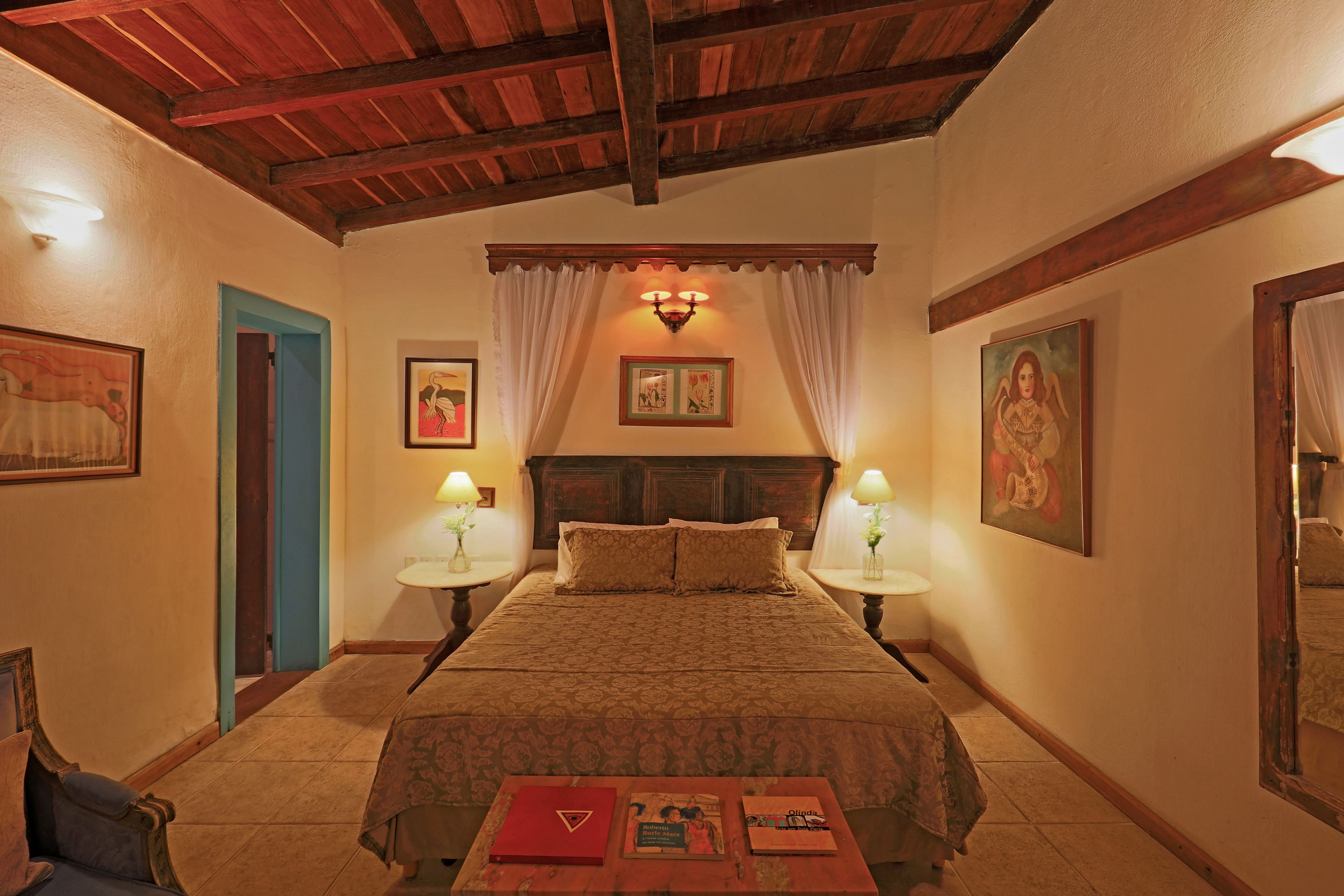 A hotel room with a large bed, two bedside tables with lamps, a wooden ceiling, and framed artwork on the walls.