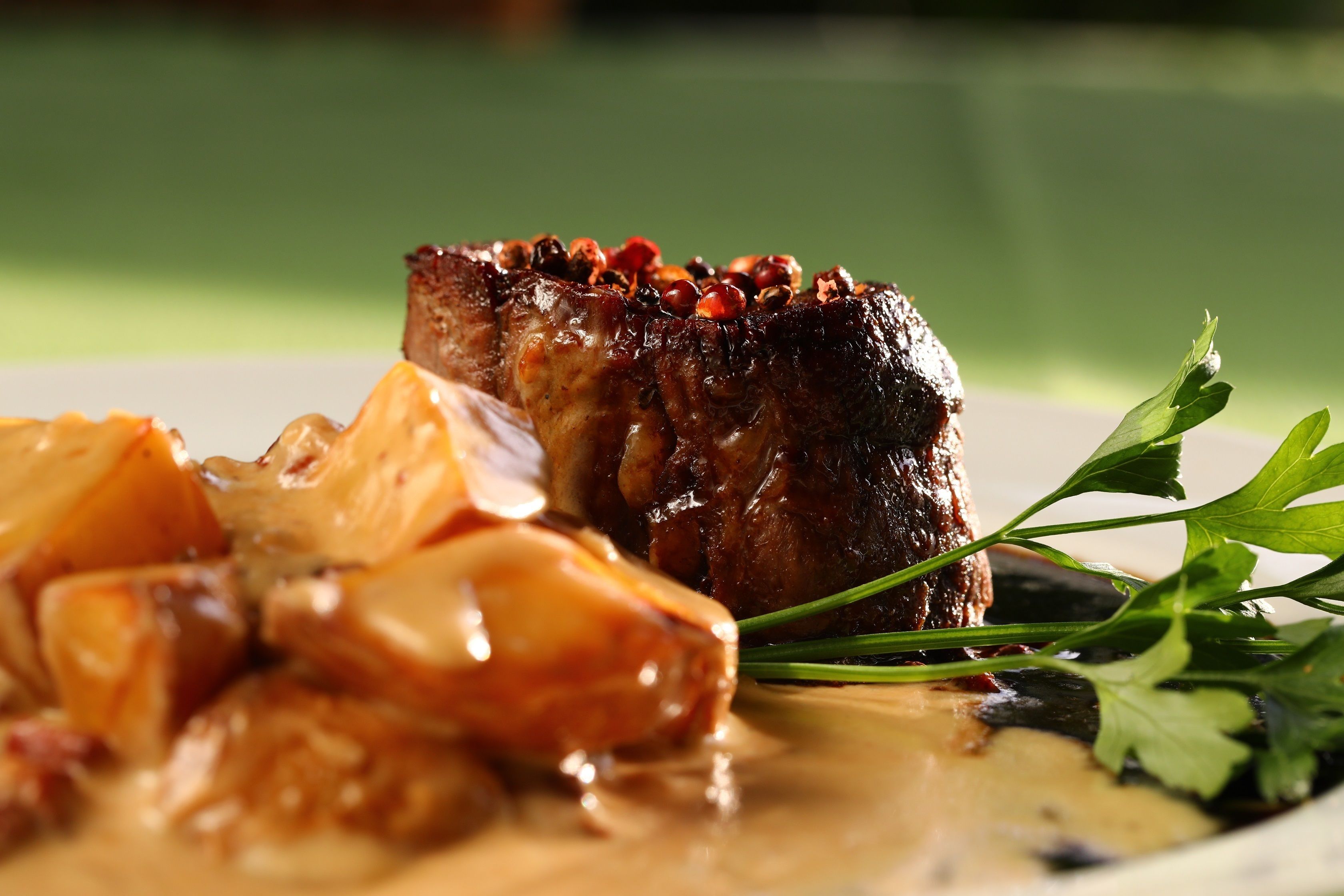 A plate with a piece of meat, potatoes, and a garnish.