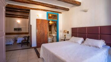 A bedroom with a large bed, a wooden door, a small table with a lamp, and a bathroom visible through an open door.