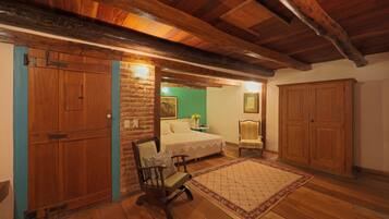 A room with wooden flooring, a bed with a green wall, a wooden rocking chair, and a large wooden wardrobe.