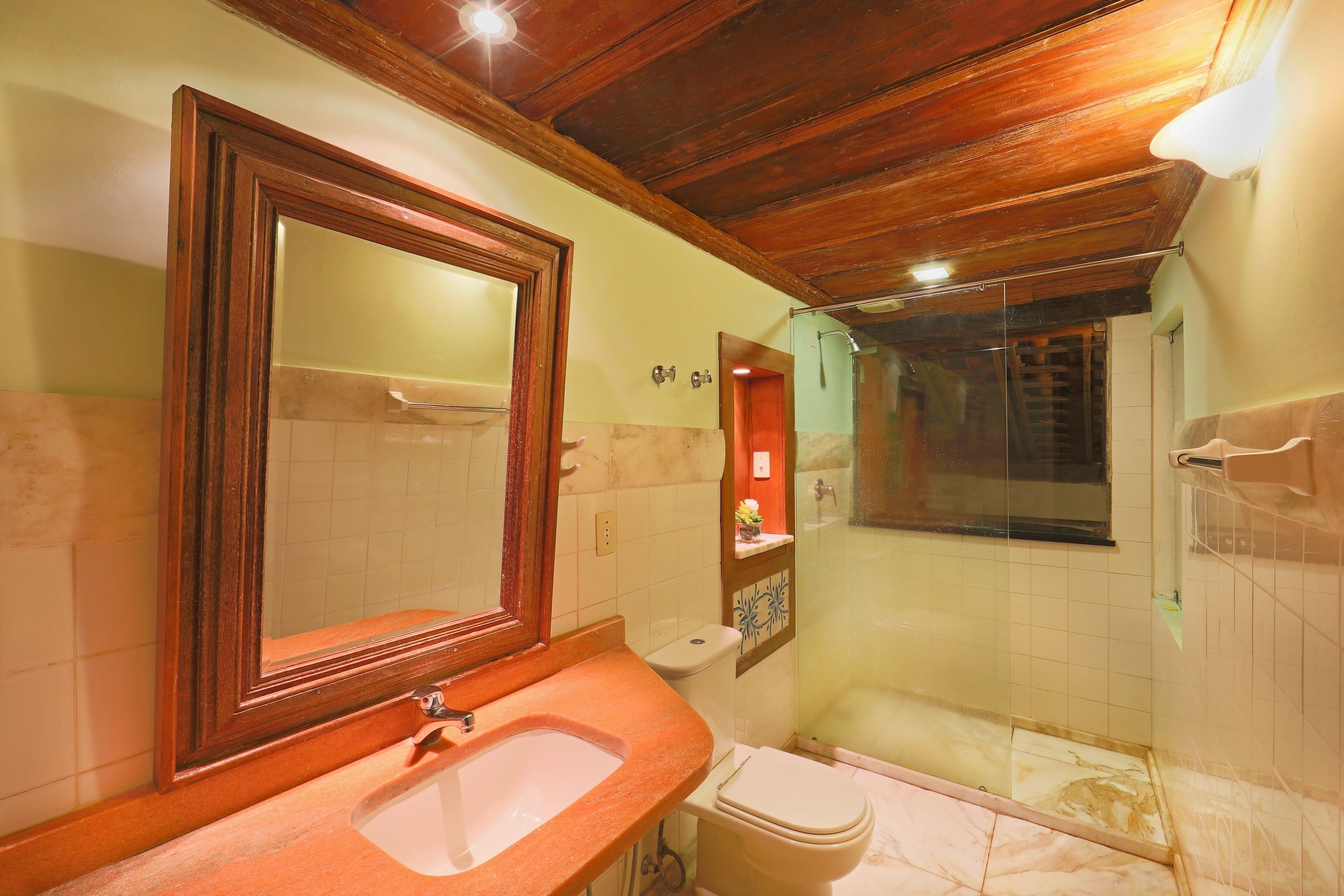 A bathroom with a wooden ceiling, a sink, a toilet, and a shower area.