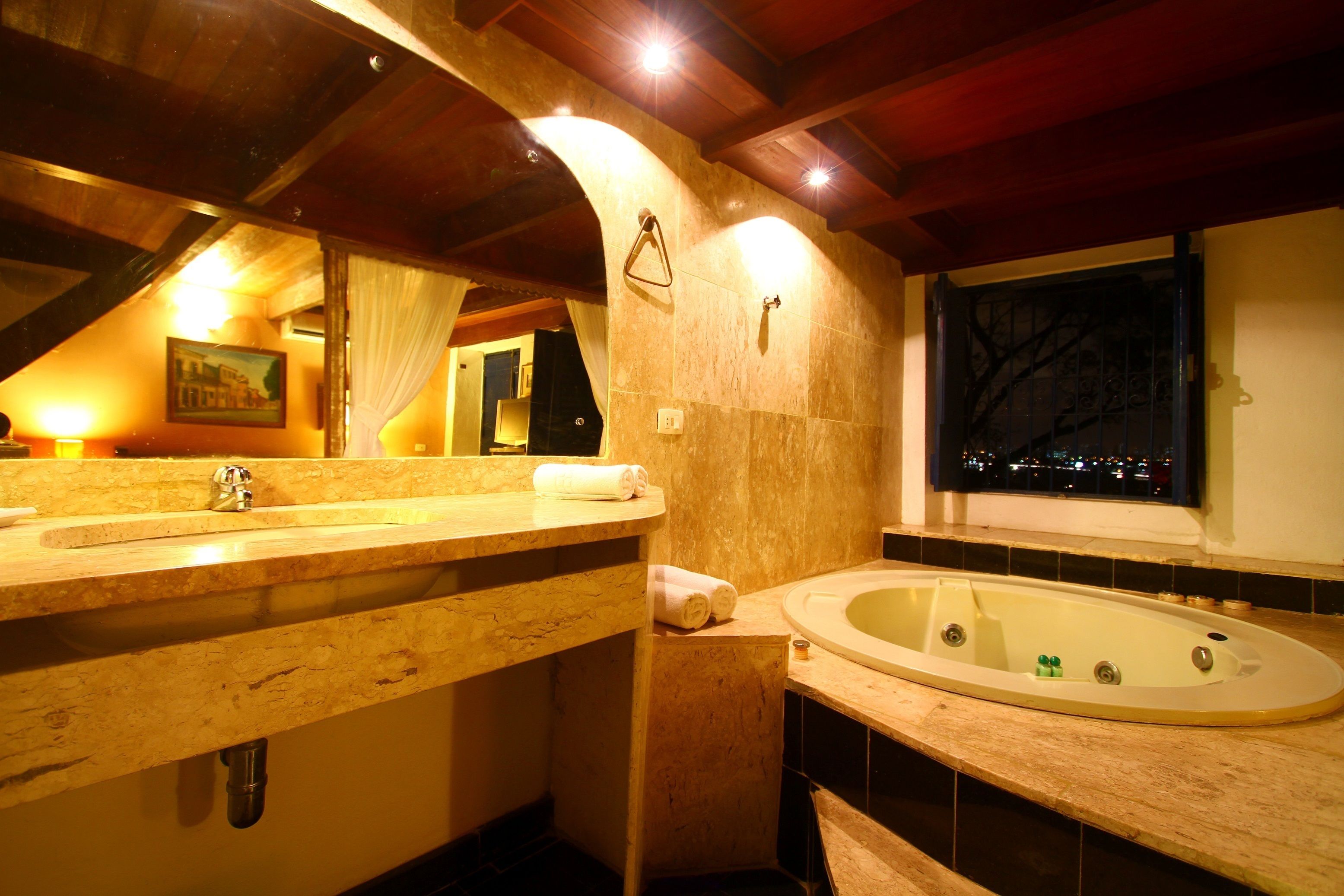A bathroom with a wooden vanity, a bathtub, and a window with a view of the city at night.