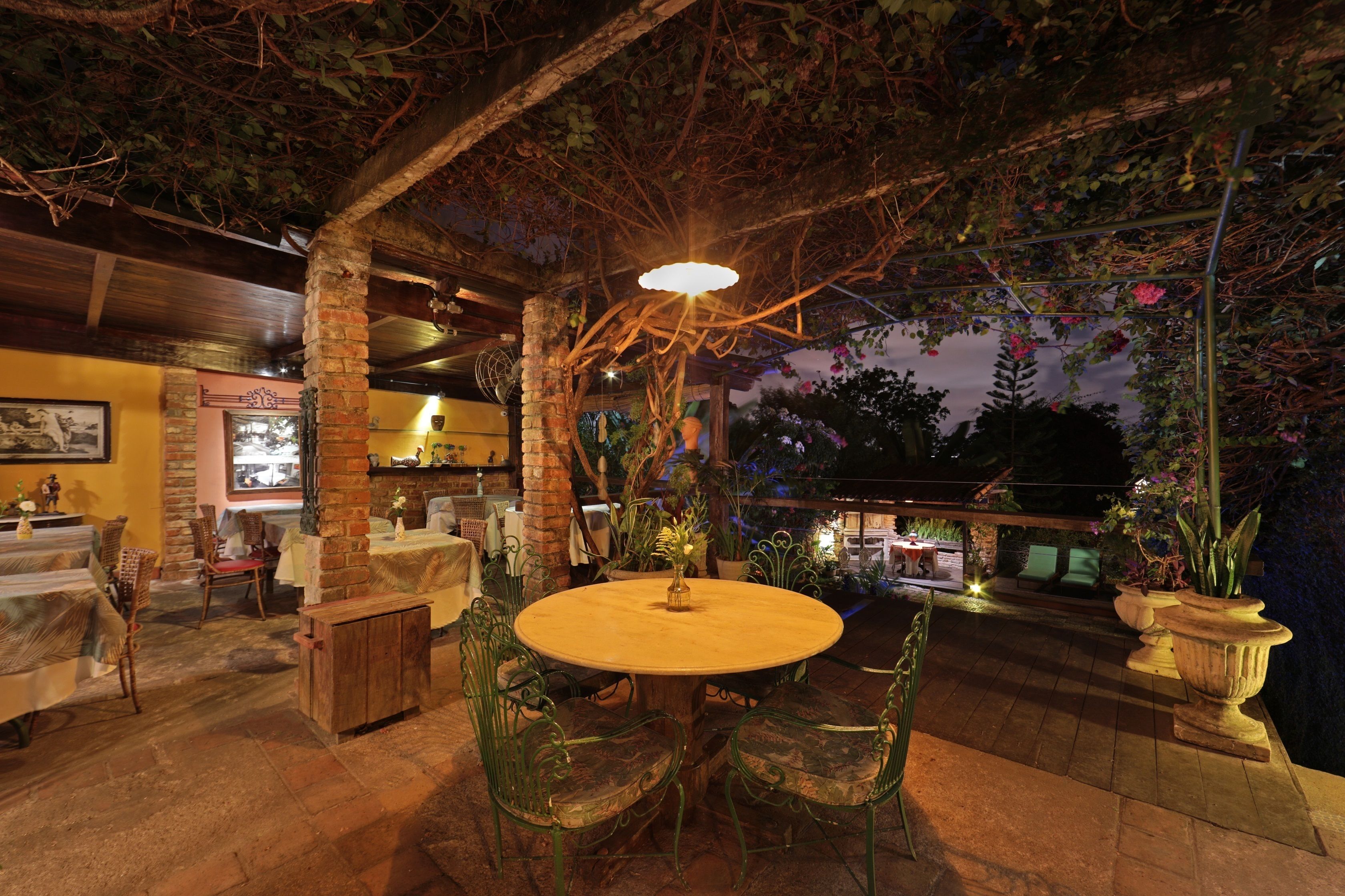 An outdoor dining area with a round table and chairs, surrounded by potted plants and a brick column.