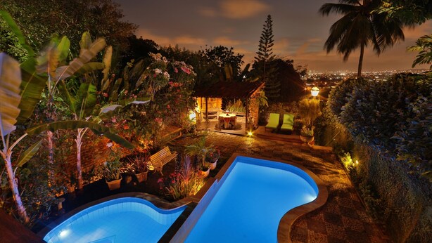 A nighttime view of a pool area with a gazebo and lounge chairs, surrounded by lush vegetation and a cityscape in the background. - Pousada do Amparo (Olinda)