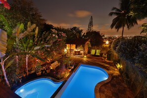 A nighttime view of a pool area with a gazebo and lounge chairs, surrounded by lush vegetation and a cityscape in the background. - Pousada do Amparo (Olinda)