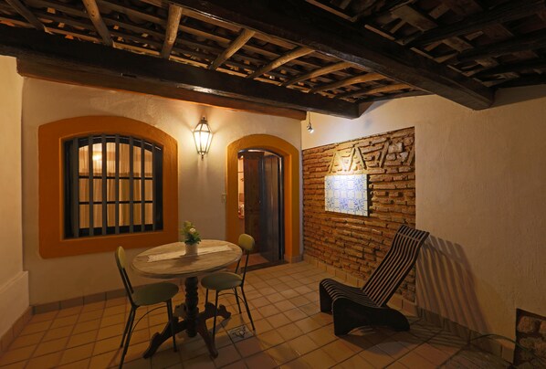 A dining area with a round table, two chairs, a potted plant, and a brick wall with a window. - Pousada do Amparo (Olinda)