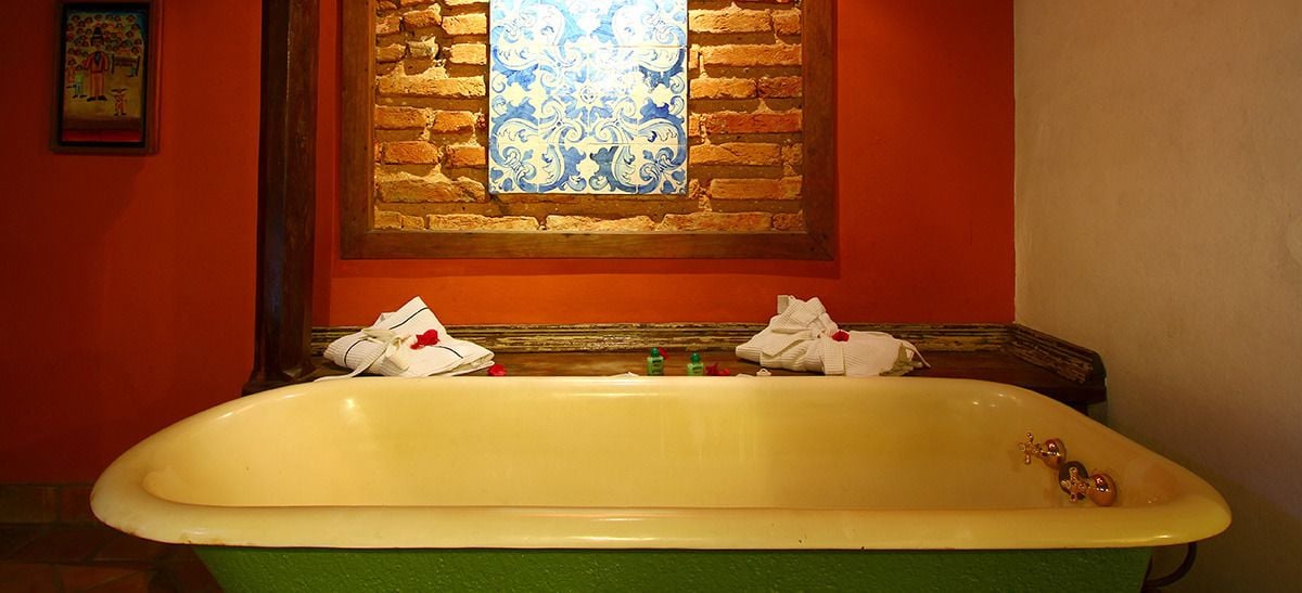 A bathtub with a green base and white interior, positioned in front of a brick wall with a decorative window above.