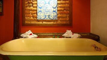 A bathtub with a green base and white interior, positioned in front of a brick wall with a decorative window above.