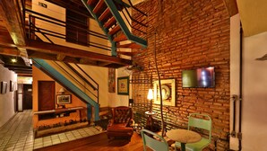 A room with a brick wall, a wooden staircase, a flat-screen TV, and a table with chairs. - Pousada do Amparo (Olinda)