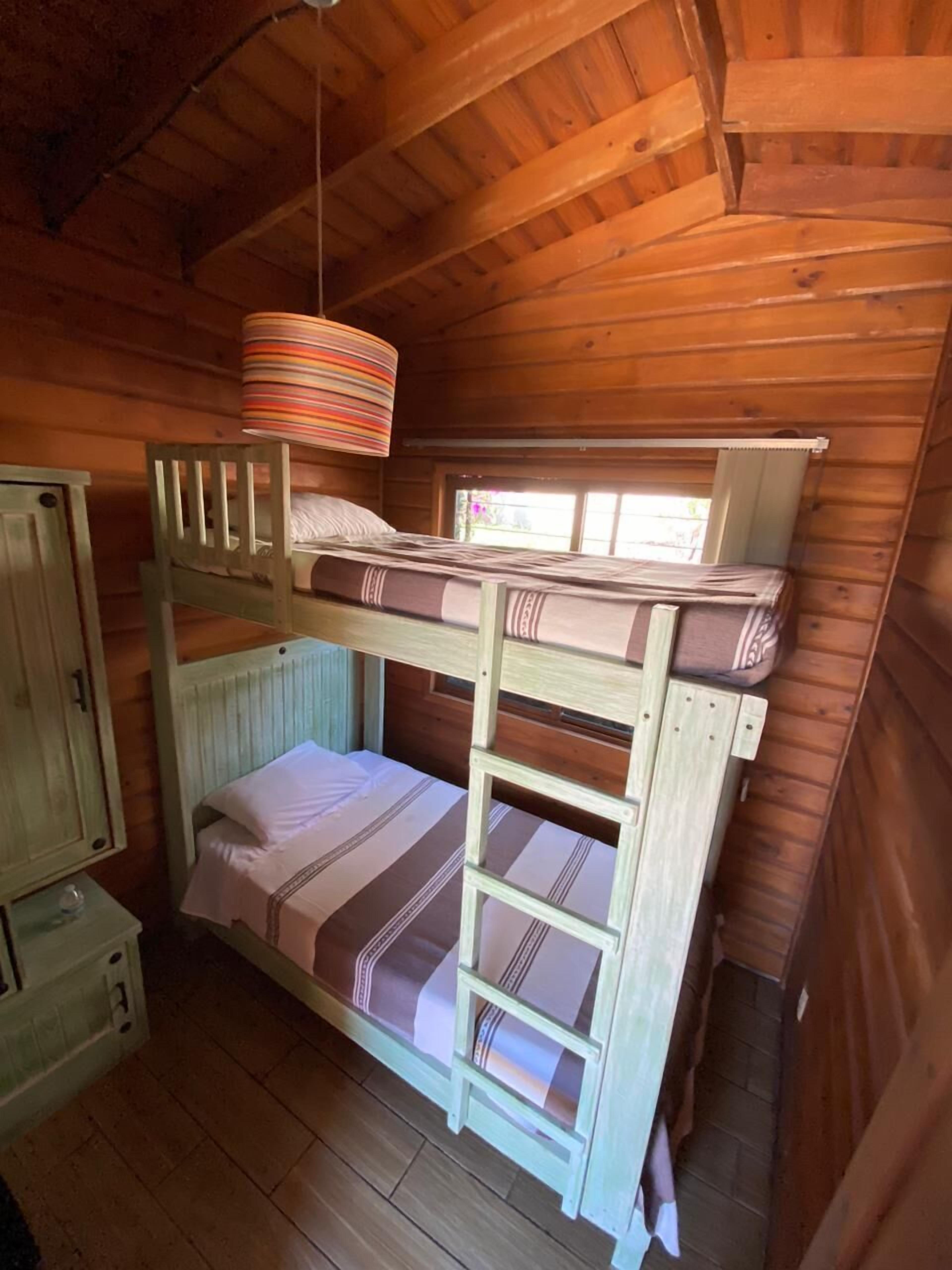 Quarto com beliche, paredes de madeira e ventoinha no teto.