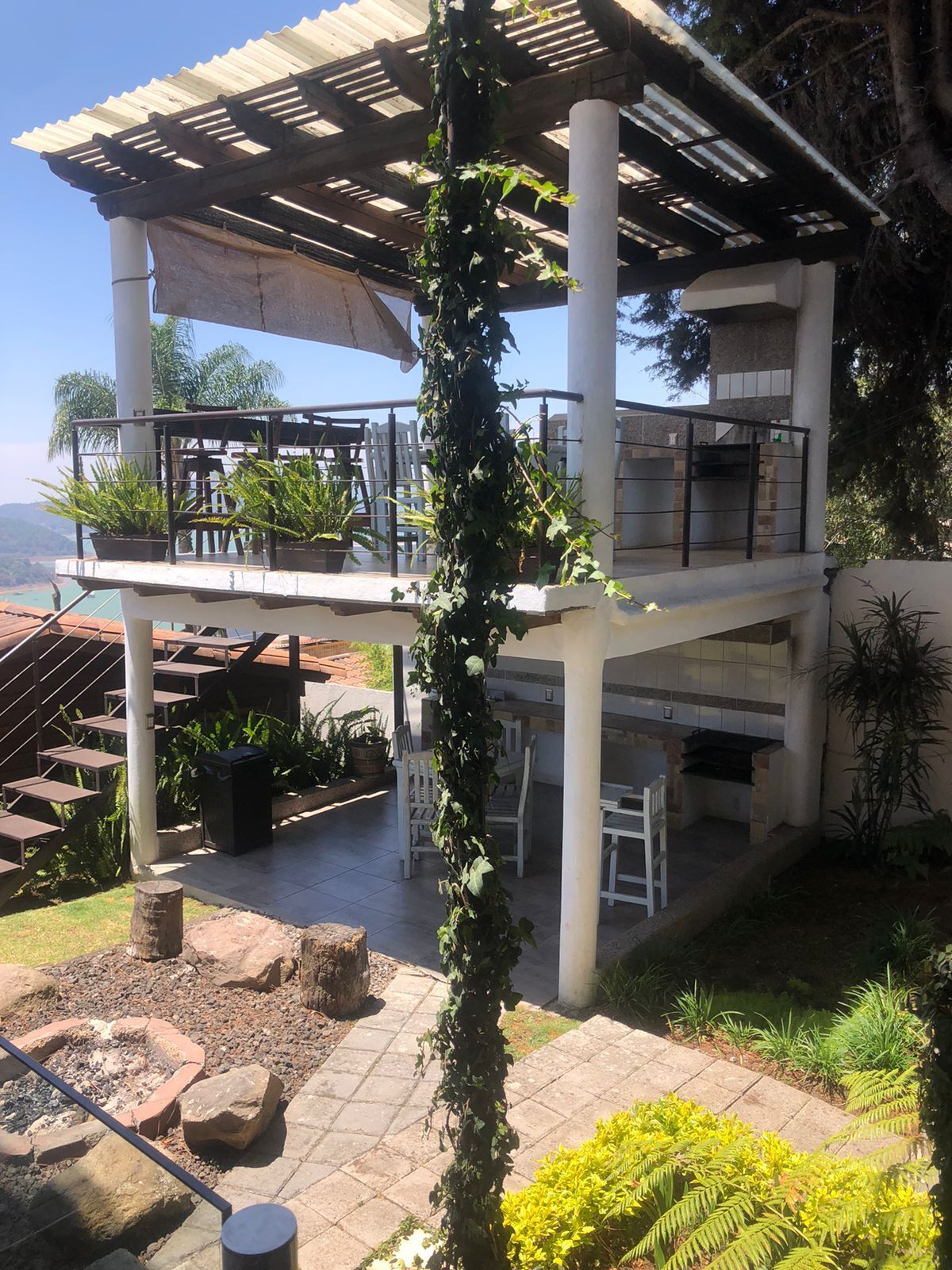 Un patio exterior cubierto con una pérgola, zona de estar y una chimenea.