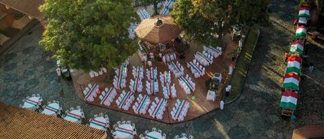 An outdoor seating area with round tables and chairs, surrounded by trees and a central gazebo.