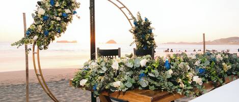 Decoración de boda en la playa con un arco de madera adornado con flores y un banco.