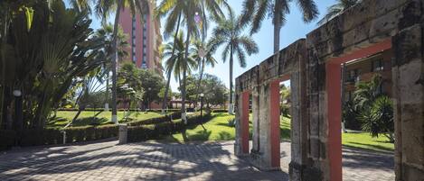 A paved pathway leading to a building with red columns, surrounded by palm trees and greenery.