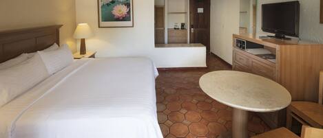 A hotel room with a large bed, a desk, a chair, a television, and a bathroom visible through an open door.