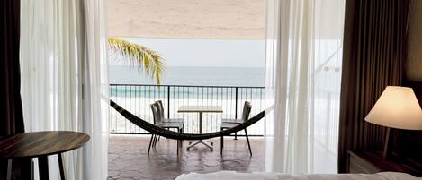 A hotel room with a bed, a table, and a hammock overlooking a beach.