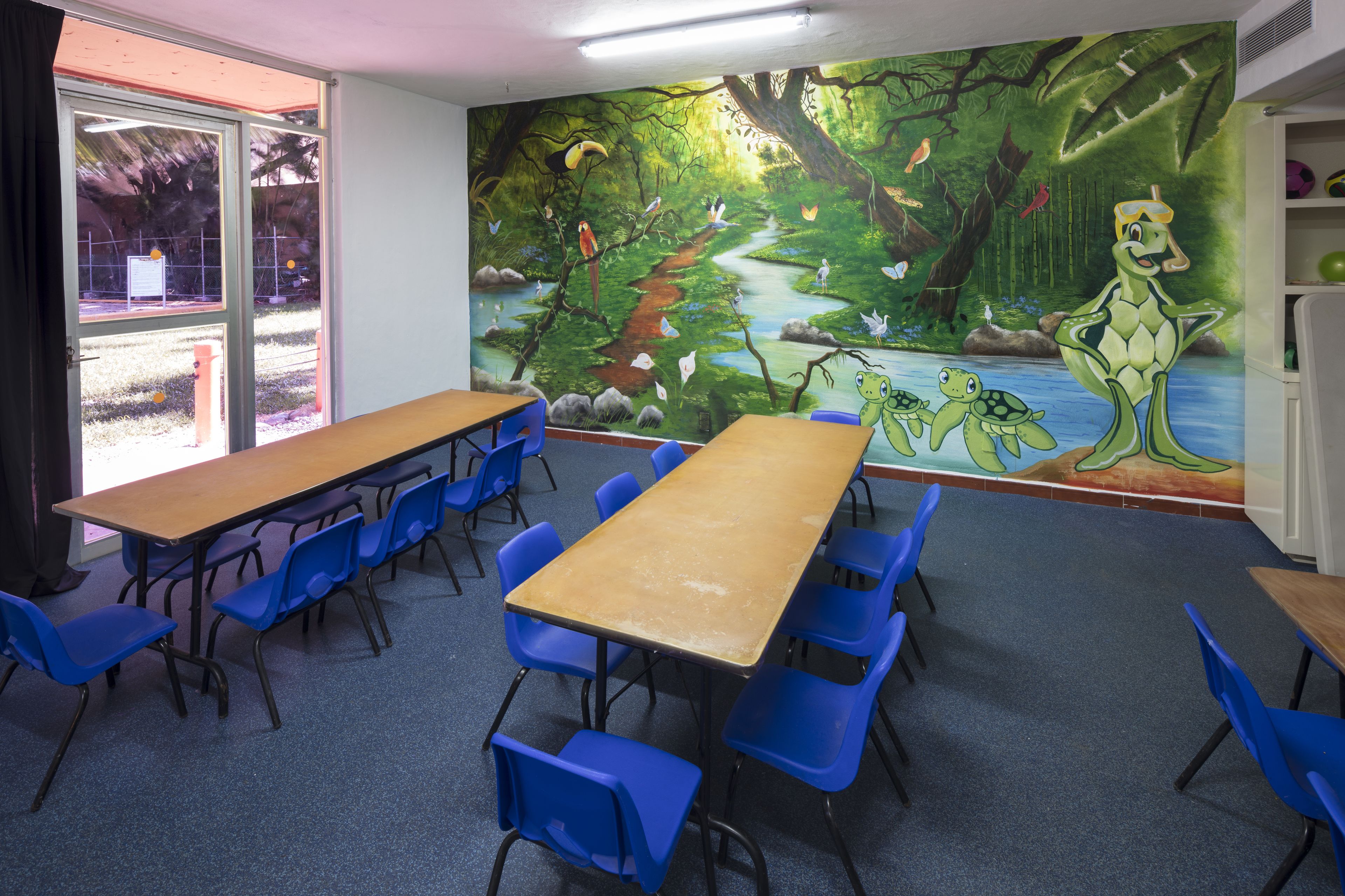 A classroom with a mural of a forest scene, blue chairs, and a long wooden table.