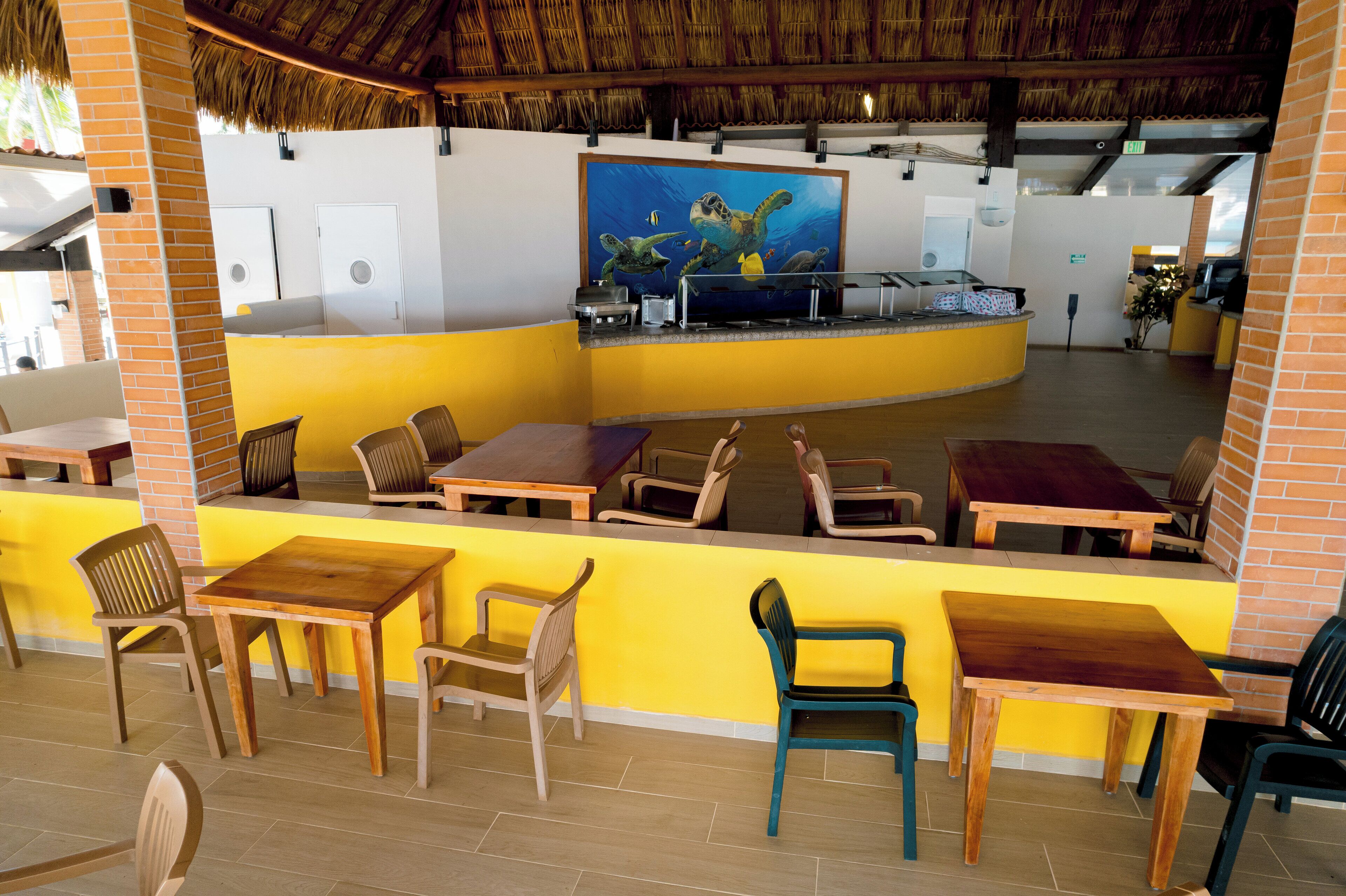 Un restaurante con mesas y sillas de madera, una pared de acento amarilla y un mural de tortugas marinas.