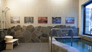 A modern bathroom with a stone wall, a small wooden stool, a bathtub, and a window. - CHIKUYOAN (Nagaokakyo)