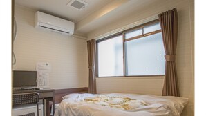 Quarto de hotel com cama, escrivaninha com computador, ar condicionado e janela com cortinas.