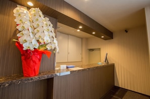A reception area with a marble counter, a red flower arrangement, and a wooden panel wall.