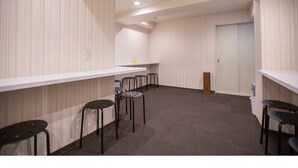 Um quarto com papel de parede listrado, uma porta branca e um balcão branco comprido com bancos pretos.