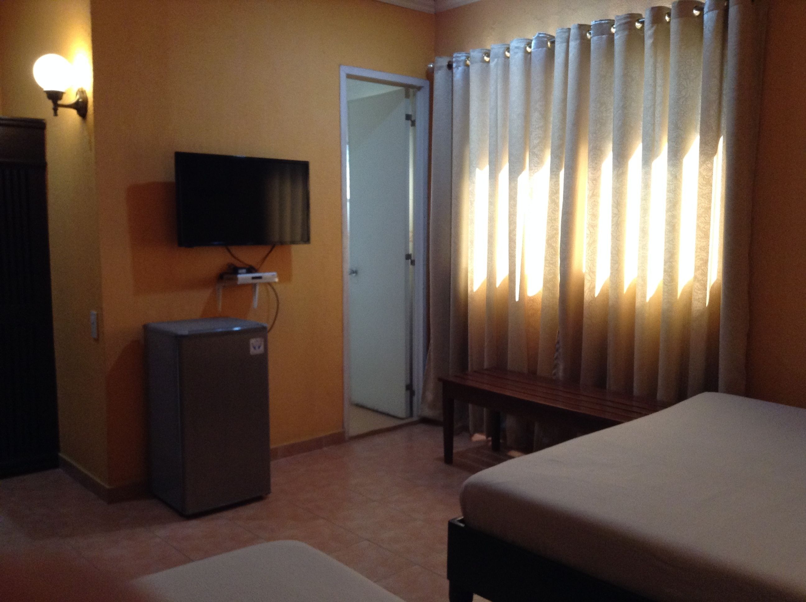 Una camera d'albergo con un letto, una televisione a parete, un piccolo armadietto e una porta.
