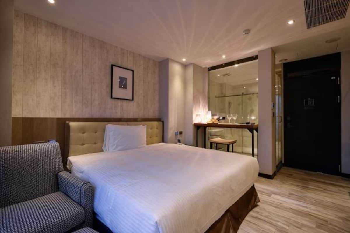 Una habitación de hotel con una cama grande, una silla, un escritorio con un espejo y una puerta.